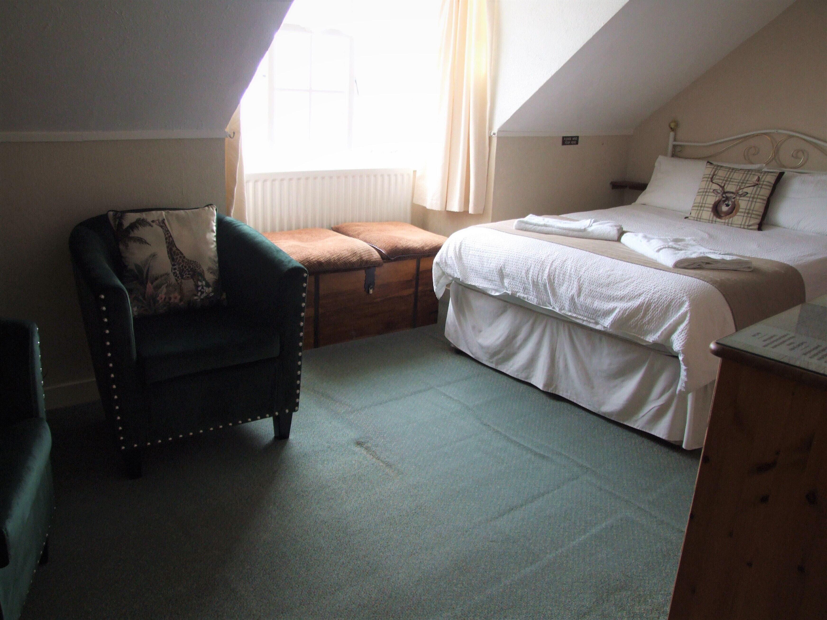 Une chambre avec un lit simple, une chaise, une commode et une fenêtre avec des rideaux.
