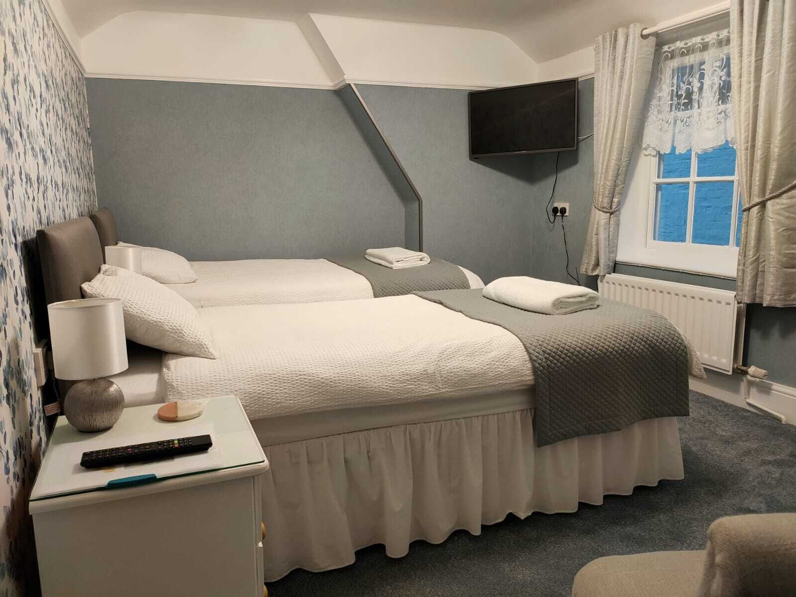 A hotel room with two beds, a TV, a desk with a lamp, and a window with curtains.