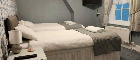 A hotel room with two beds, a TV, a desk with a lamp, and a window with curtains.