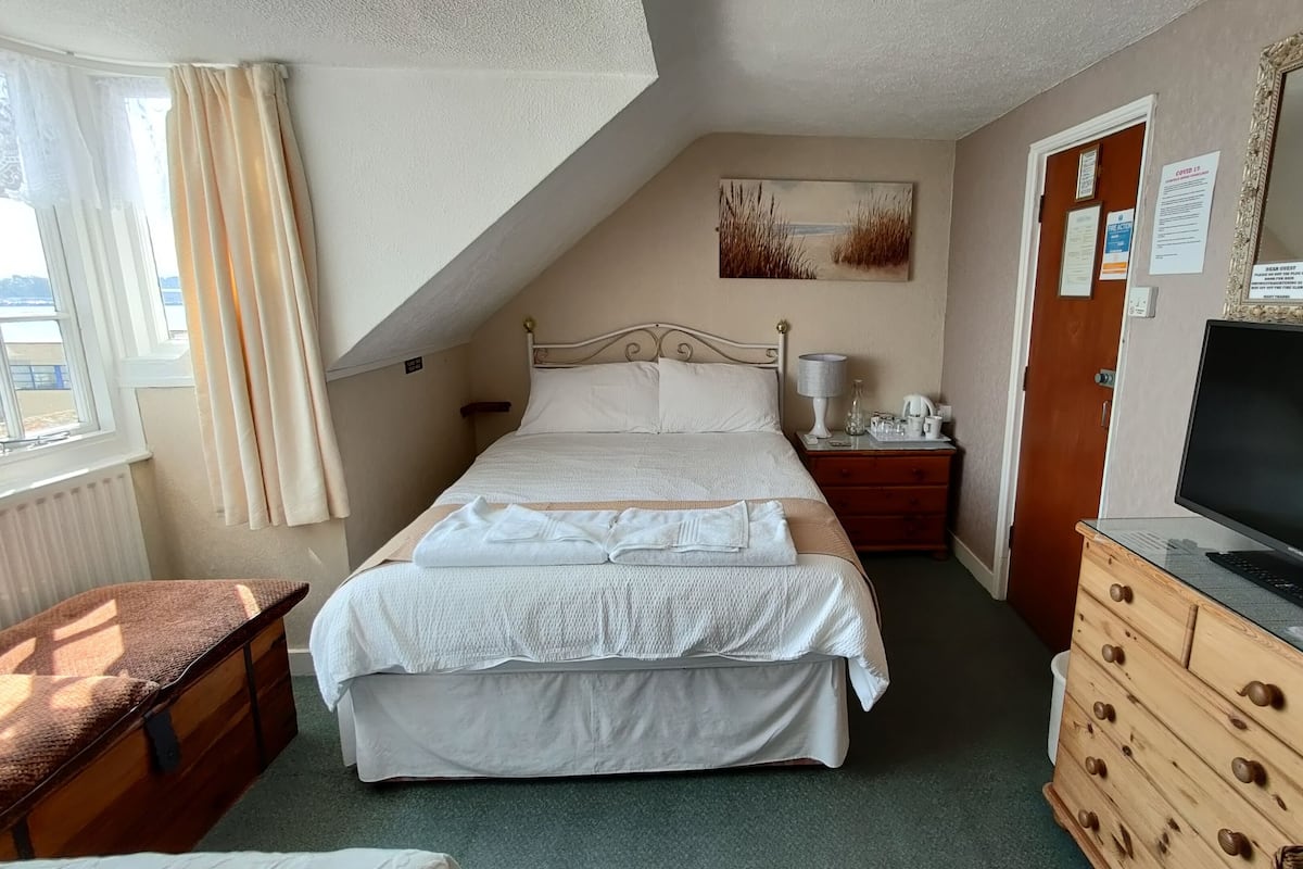 Ein ordentlich eingerichtetes Schlafzimmer mit Bett, Nachttisch, Lampe, Kommode und Fernseher.