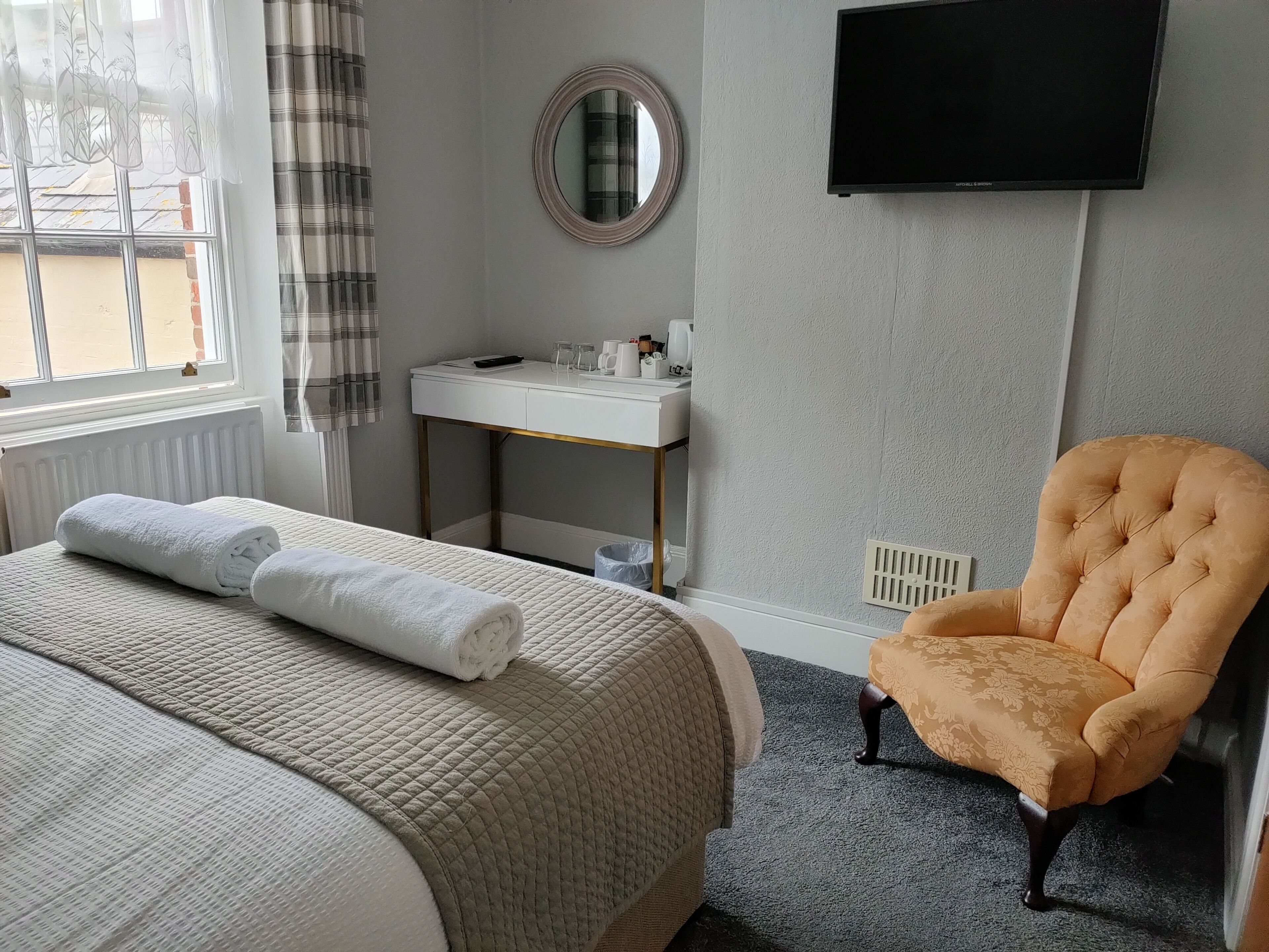 A hotel room with a bed, a chair, a desk with a mirror, and a television on the wall.