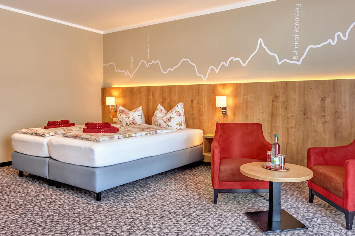Ein Hotelzimmer mit einem Bett, zwei roten Sesseln, einem kleinen Tisch und einer Wand mit einem Liniendiagramm.