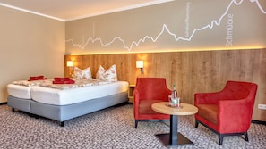 A hotel room with a bed, two red armchairs, a small table, and a wall with a line graph. - Hotel Traumblick (Oberhof)