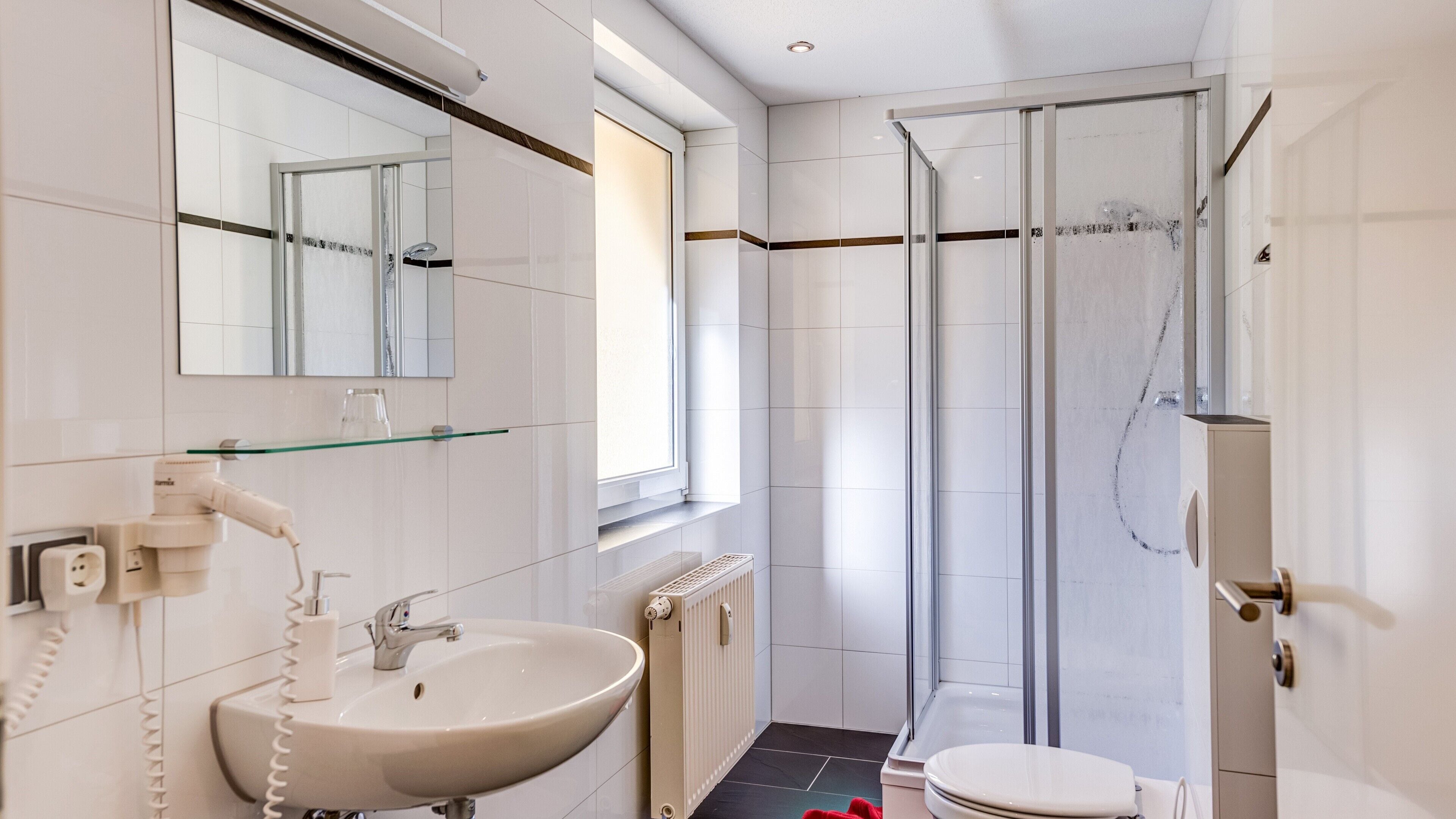 Ein modernes Badezimmer mit Duschkabine aus Glas, einem weißen Waschbecken und einer Toilette.