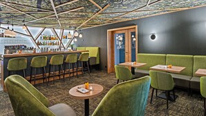 Zona de bar moderna con asientos tapizados en verde, una barra con gran variedad de botellas y un techo con diseño geométrico.