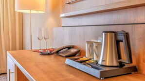 Habitación de hotel con un escritorio de madera, un teléfono, dos copas de vino, una cafetera y una bandeja con comida.