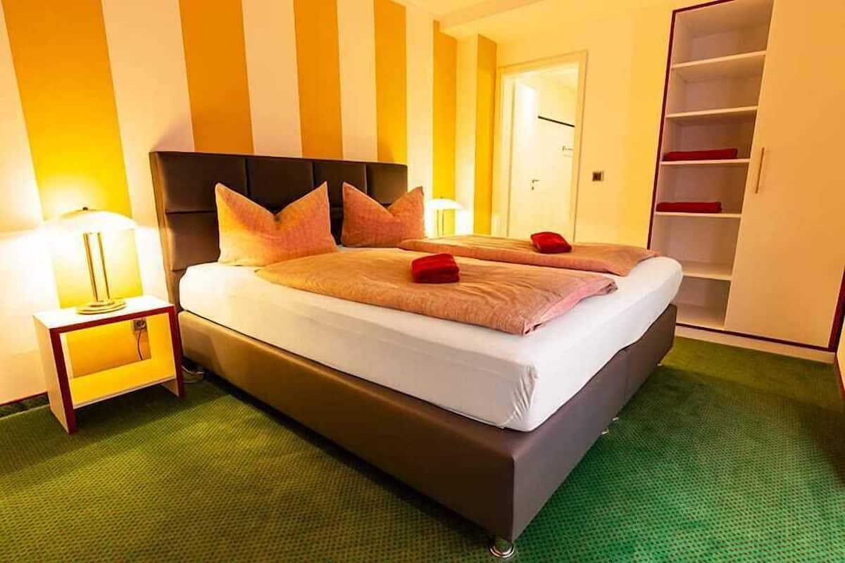 Ein Hotelzimmer mit einem großen Bett, einem Nachttisch, einer Lampe und einem Kleiderschrank.
