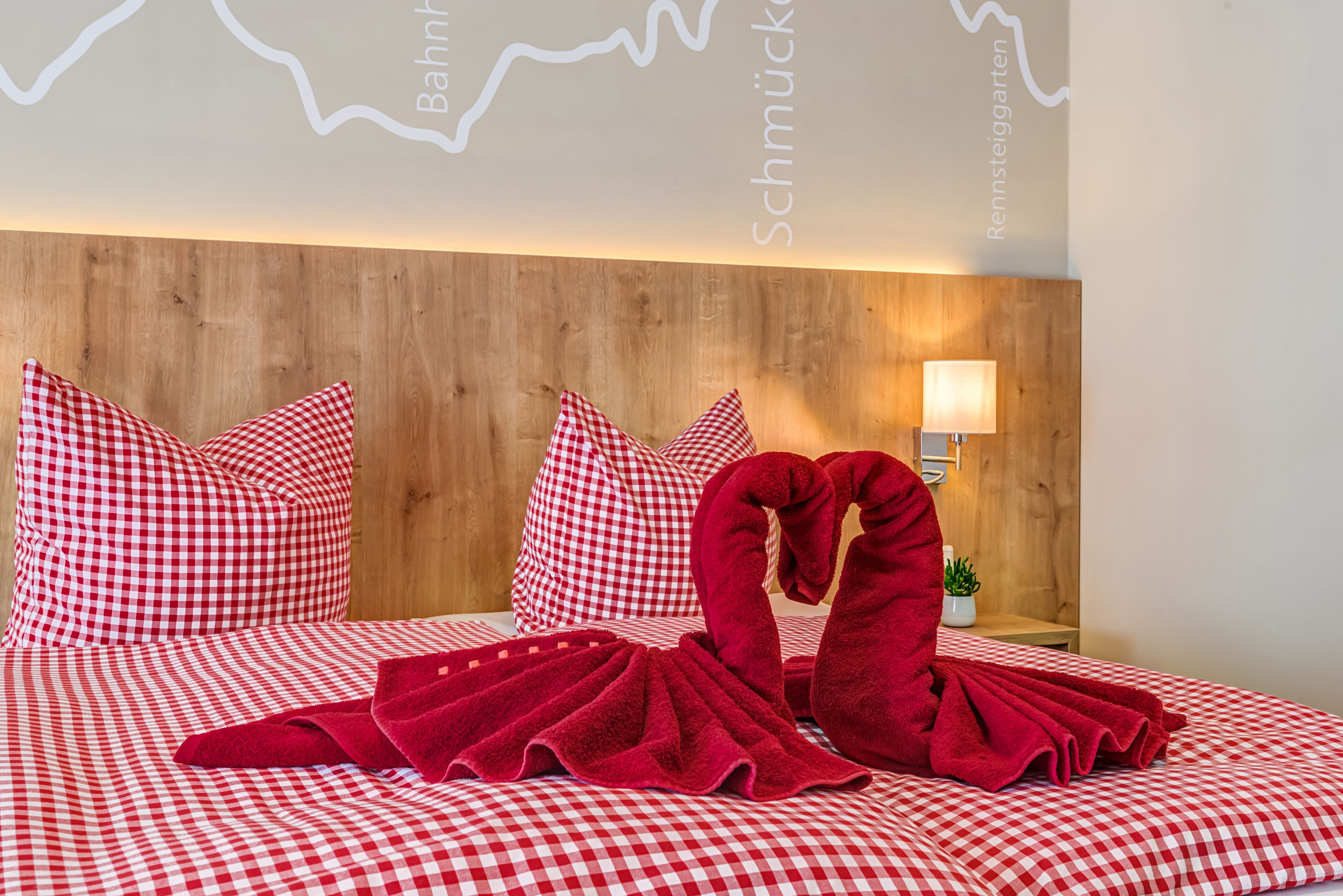 Ein Hotelzimmer mit Holz-Kopfteil, karierter Bettwäsche und einer roten Handtuchskulptur.