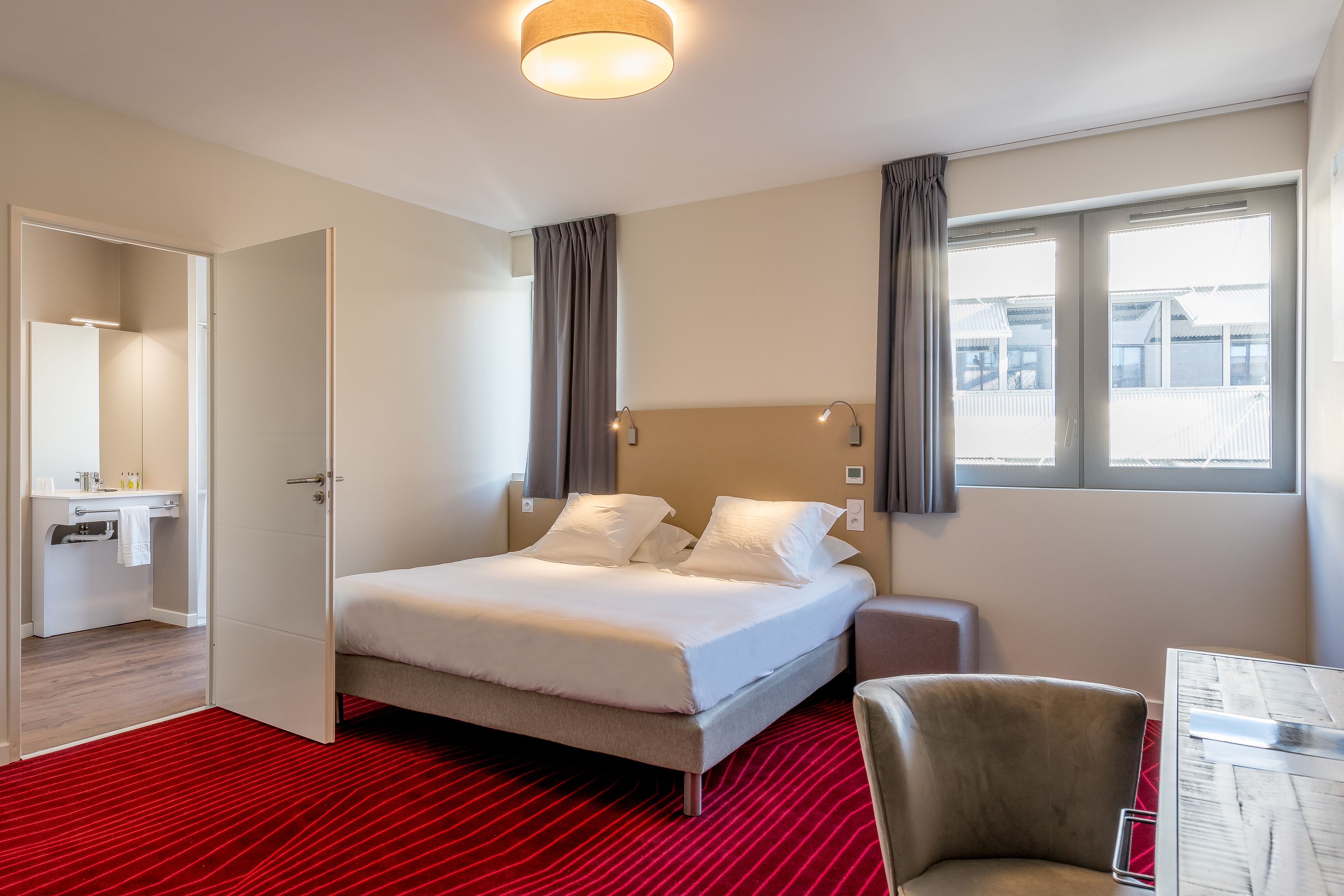 Habitació d'hotel amb un llit, escriptori, cadira i finestra amb cortines.