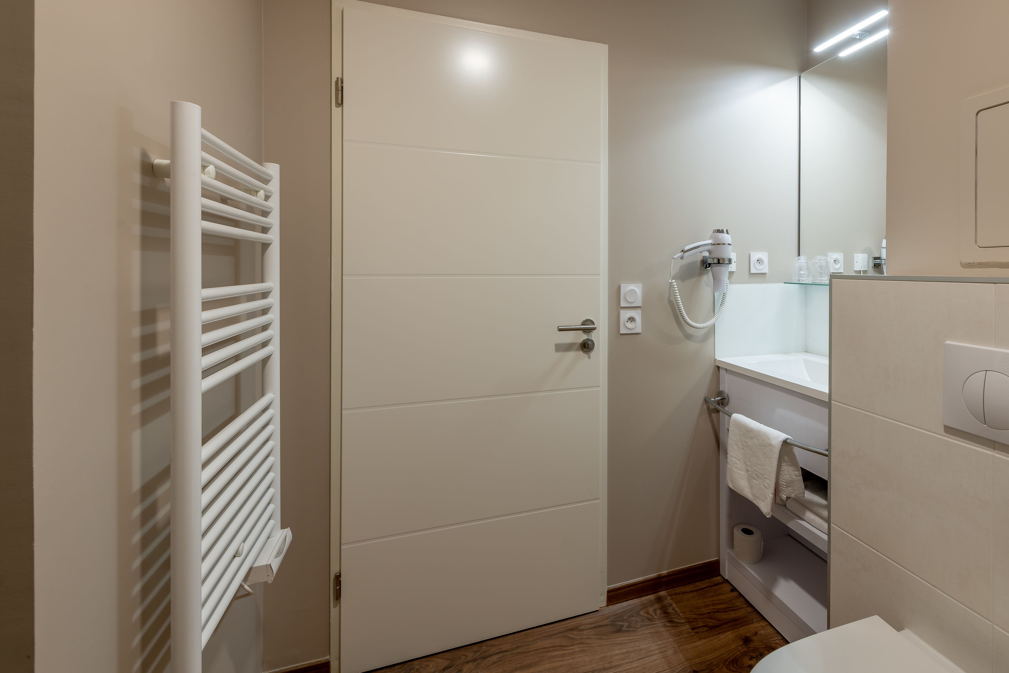 Un baño con una puerta blanca, un perchero para toallas, una ducha con cabezal de ducha manual y un inodoro.