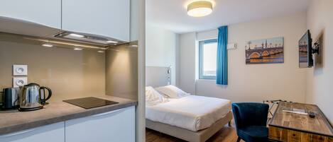 Una habitación de hotel compacta con kitchenette, una cama, un escritorio y una silla.