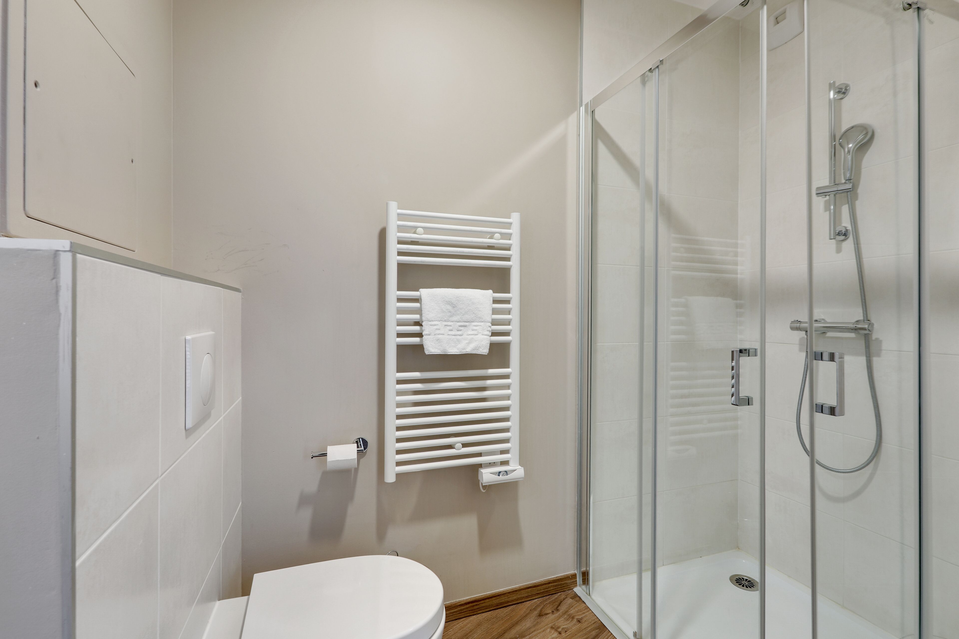 Un bagno moderno con un water, una cabina doccia in vetro e un portasciugamani bianco.