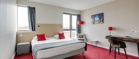 Una habitación de hotel con cama, escritorio, silla, lámpara y un cuadro en la pared.