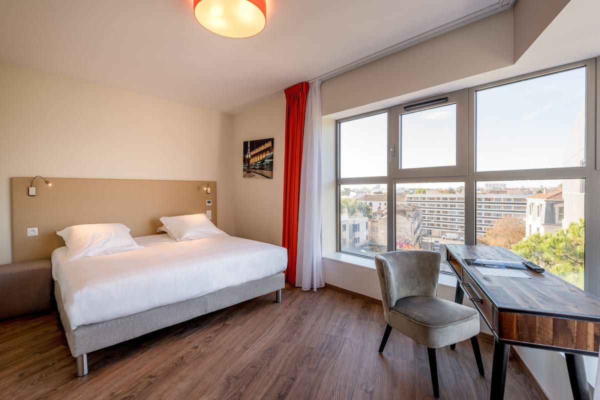 Une chambre d’hôtel avec un lit, un bureau et une chaise.