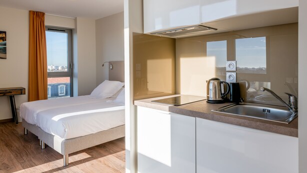 Ein Hotelzimmer mit Bett, einer Küchenzeile und einem Fenster mit Vorhängen.