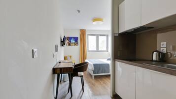 A modern hotel room with a wooden dining table, a single bed, and a kitchenette.