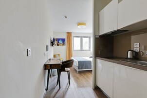 A modern hotel room with a wooden dining table, a single bed, and a kitchenette.