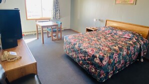 A hotel room with a bed, a desk with a telephone, a chair, a window with curtains, and a bedside table with a lamp.