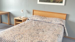 A neatly made bed with a quilted cover, a wooden headboard, and a bedside table with a lamp.