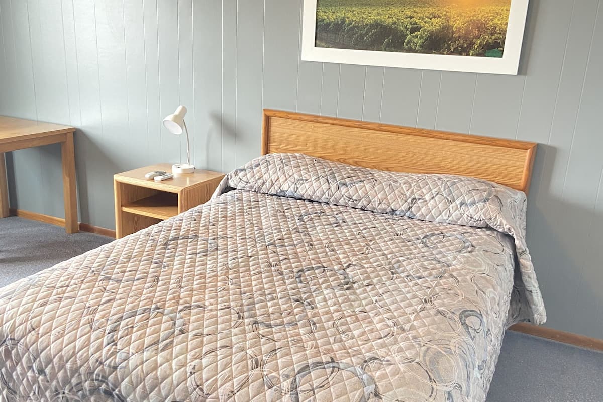 A neatly made bed with a quilted cover, a wooden headboard, and a bedside table with a lamp.