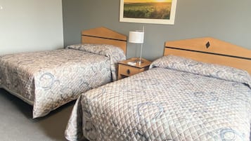 Een hotelkamer met twee bedden, een nachtkastje, een lamp en een schilderij van een ondergaande zon aan de muur.
