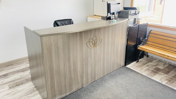 A reception desk with a logo, a computer, a printer, and a bench.