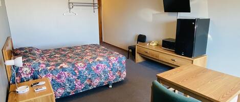 A hotel room with a bed, a desk, a chair, a television, and a wardrobe.