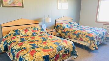 A hotel room with two beds, each with a colorful quilt, a bedside table with a lamp, and a framed picture on the wall.