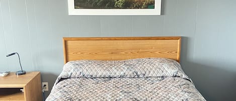 Una cama bien hecha con colcha estampada, cabecera de madera y un cuadro enmarcado con una vista de un viñedo al atardecer en la pared.