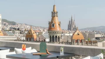 Una terraza en la azotea con una mesa preparada para dos personas, con vistas a un paisaje urbano de arquitectura singular.
