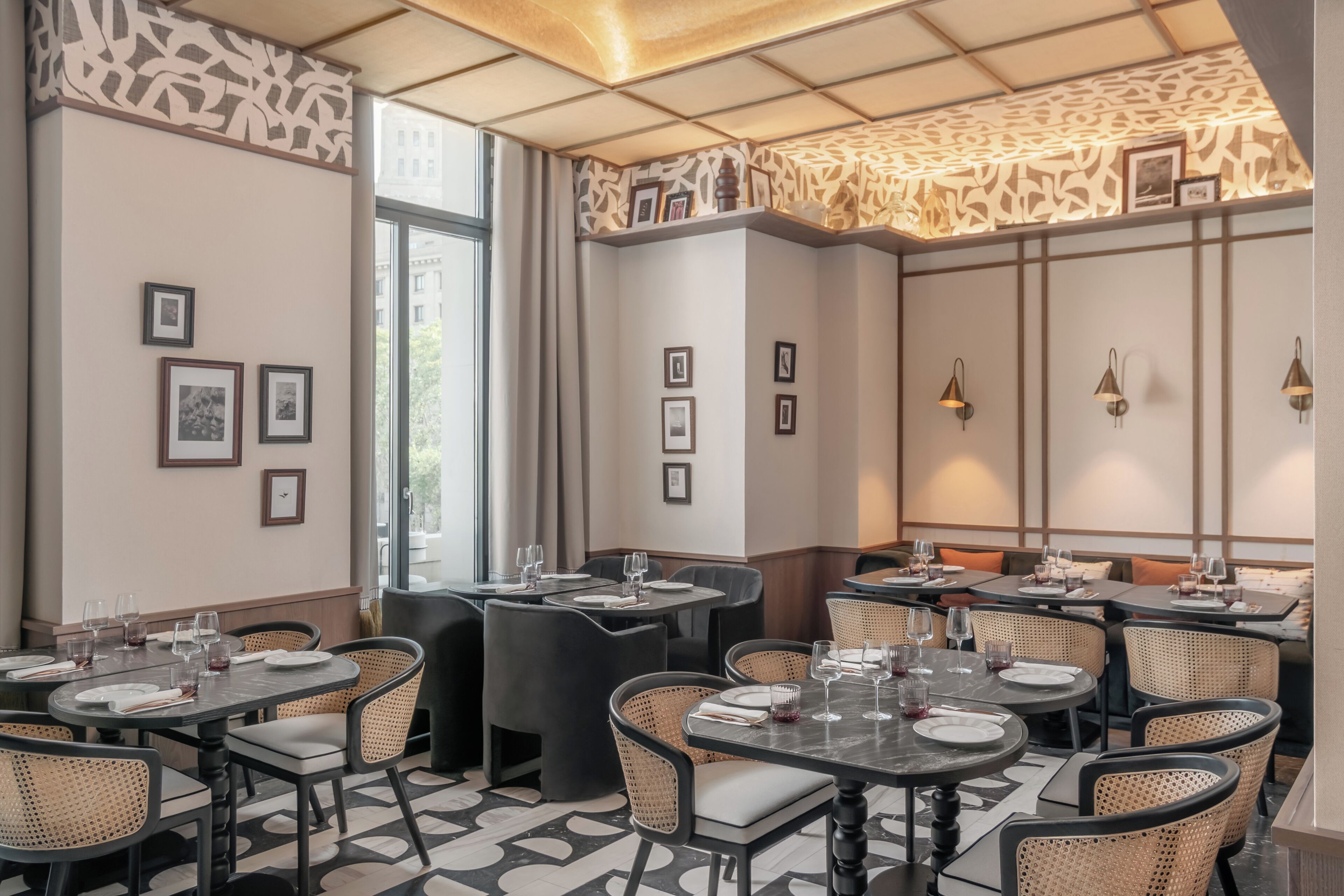 Interior de restaurante con varias mesas, sillas, cuadros en las paredes y un techo estampado.