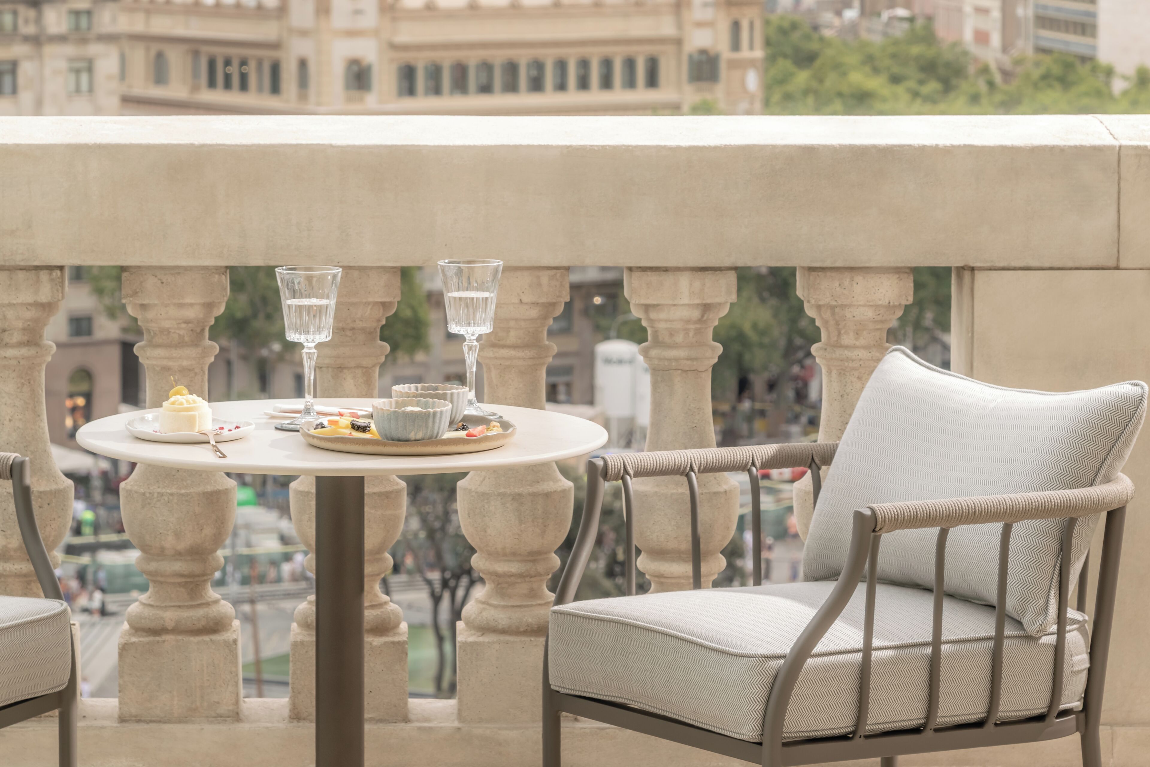 A balcony with a round table set for two, featuring a glass of water, a plate with food, and a cup.