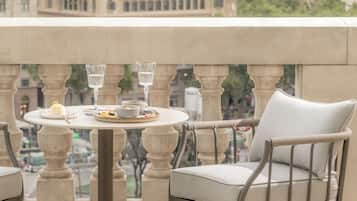 A balcony with a round table set for two, featuring a glass of water, a plate with food, and a cup.