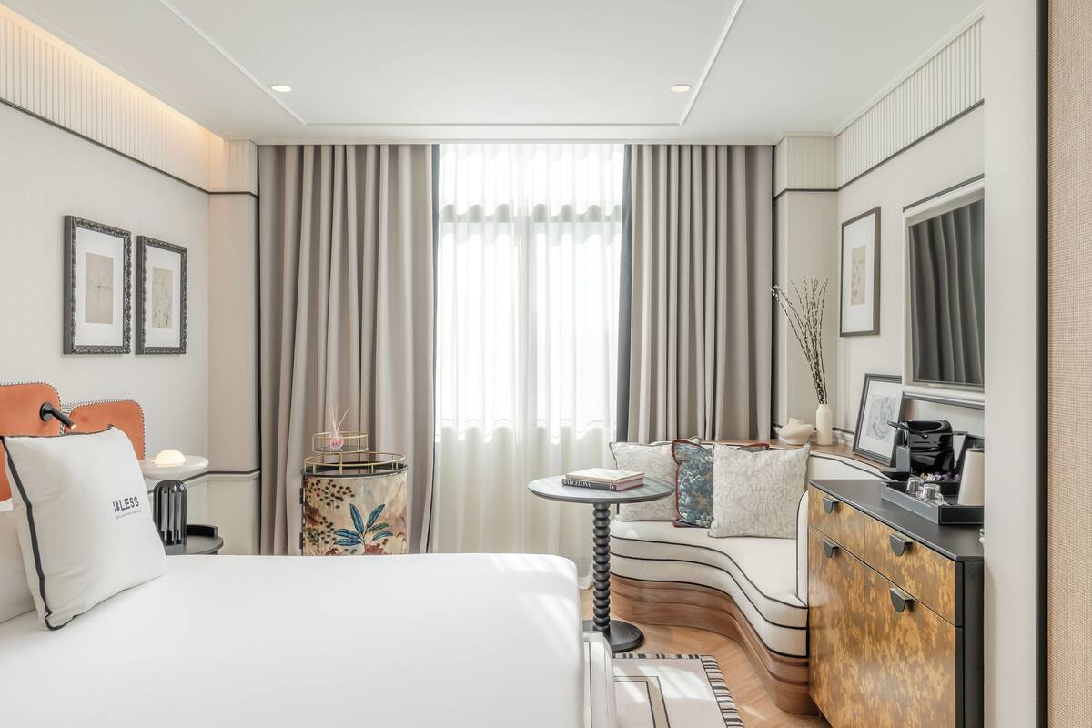 Ein modernes Hotelzimmer mit einem großen Bett, einer gebogenen Sitzecke, einem kleinen runden Tisch und einer Minibar.