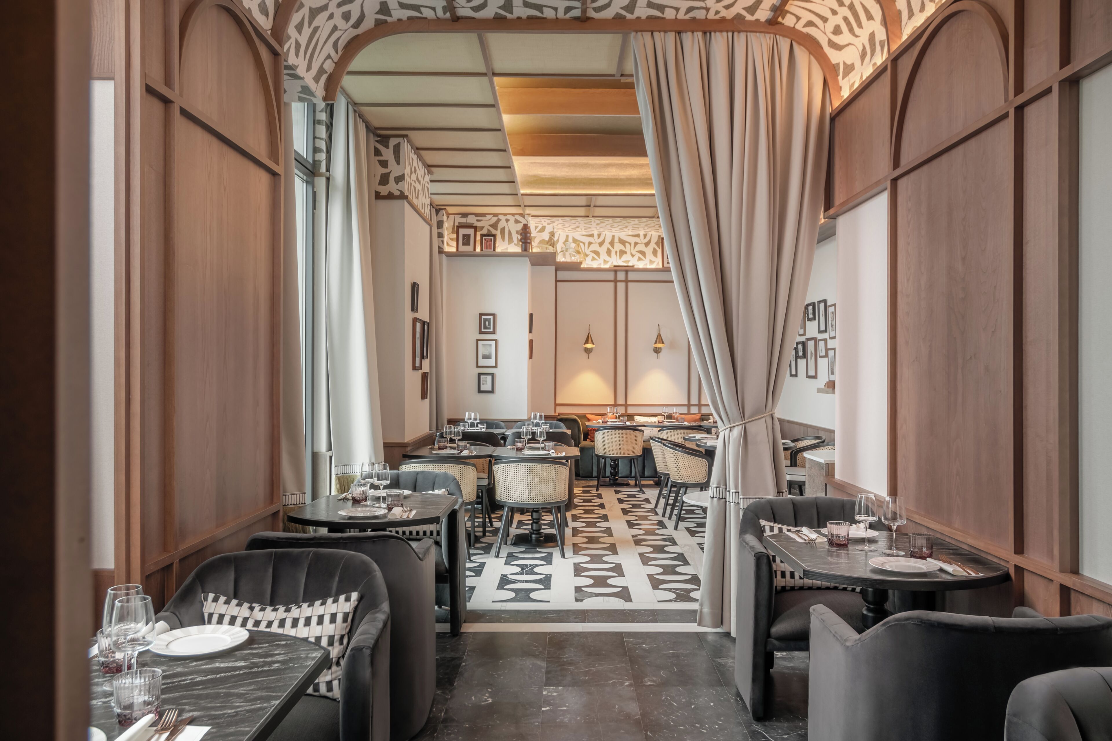 A restaurant with a modern interior, featuring a central seating area with round tables and chairs, a patterned floor, and a decorative ceiling.