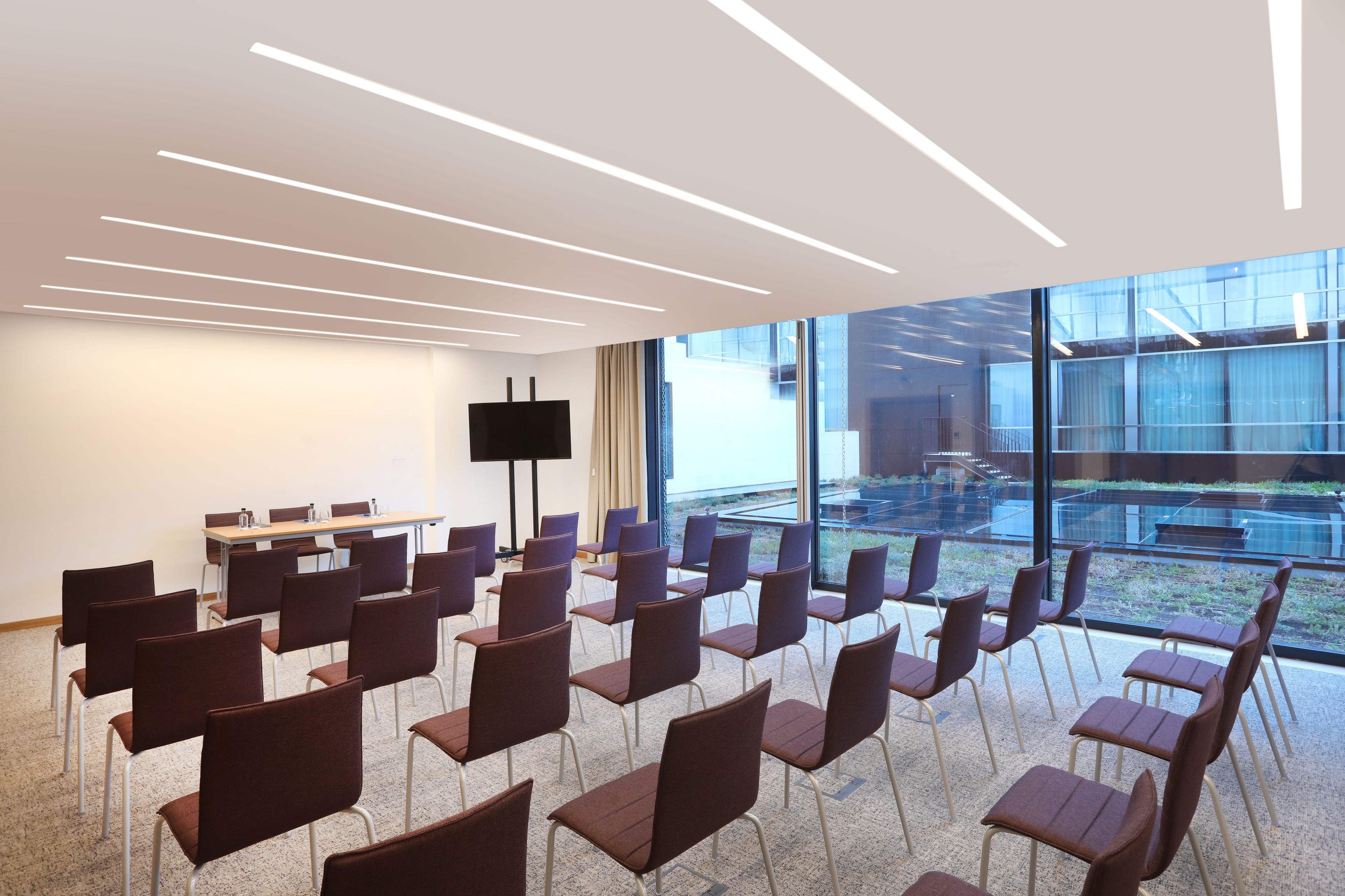 Un salón de conferencias con filas de sillas, una mesa grande y una televisión de pantalla plana.