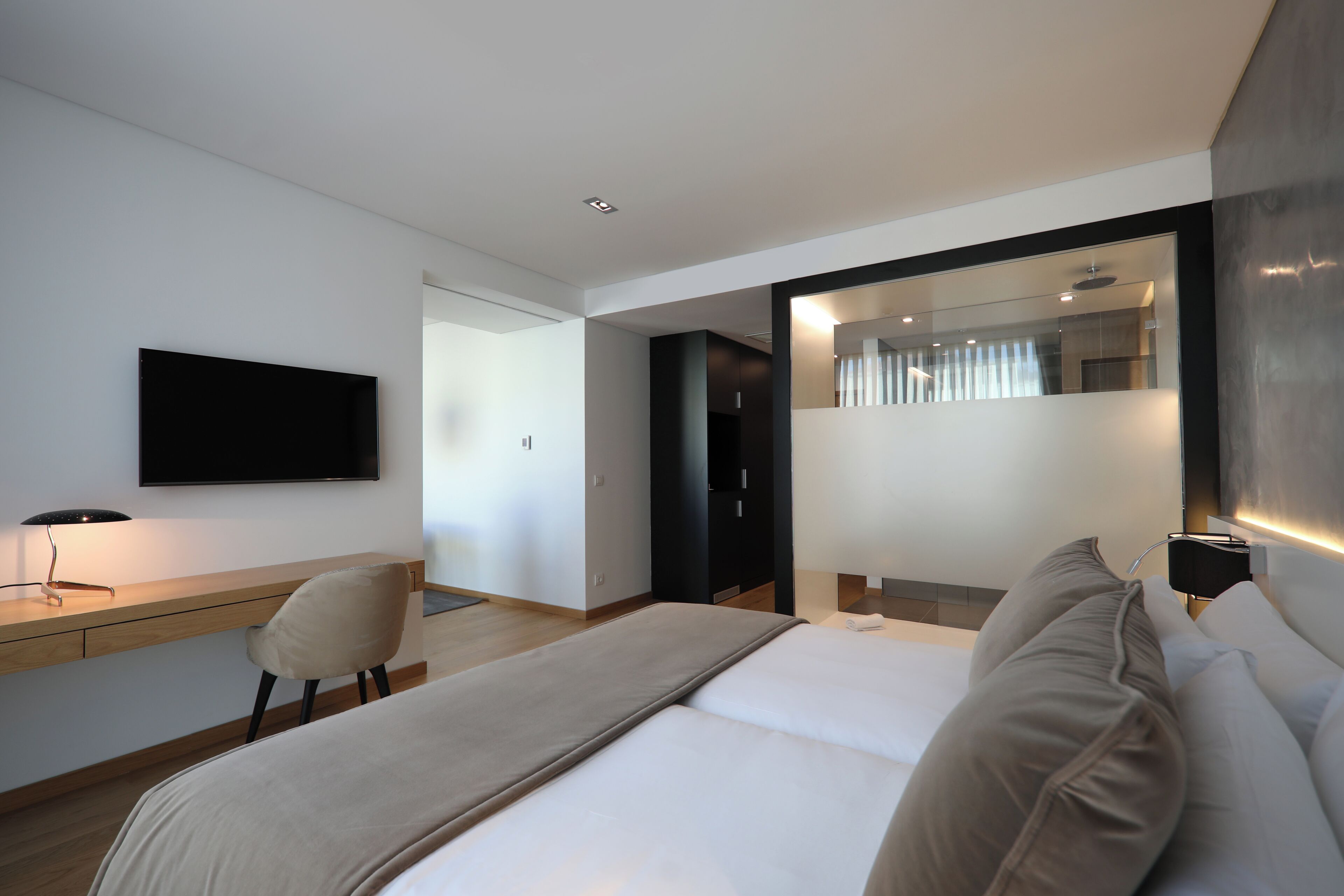 A modern hotel room with a bed, a desk, a chair, a flat-screen TV, and a mirror.