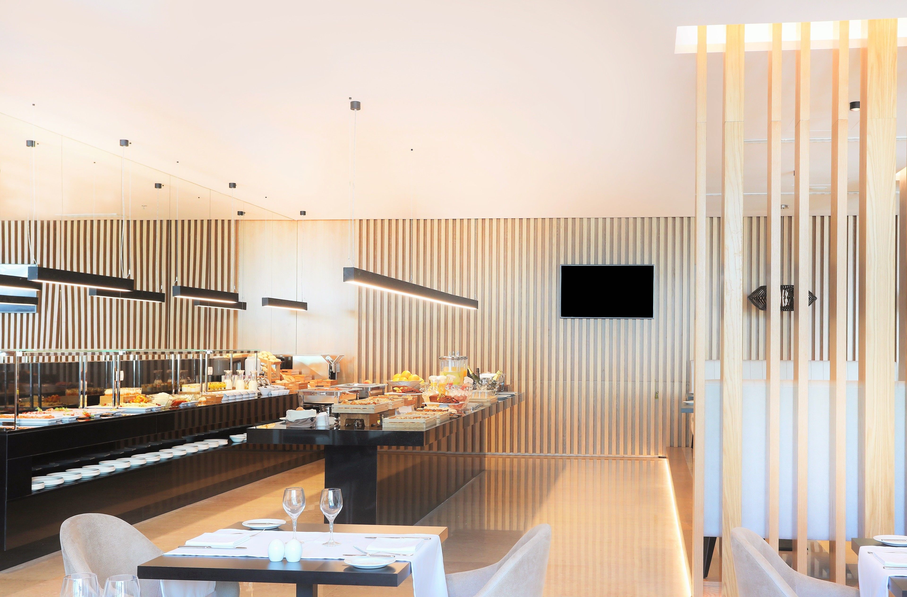 A modern dining area with a buffet setup, a flat-screen TV mounted on the wall, and a wooden partition with vertical slats.