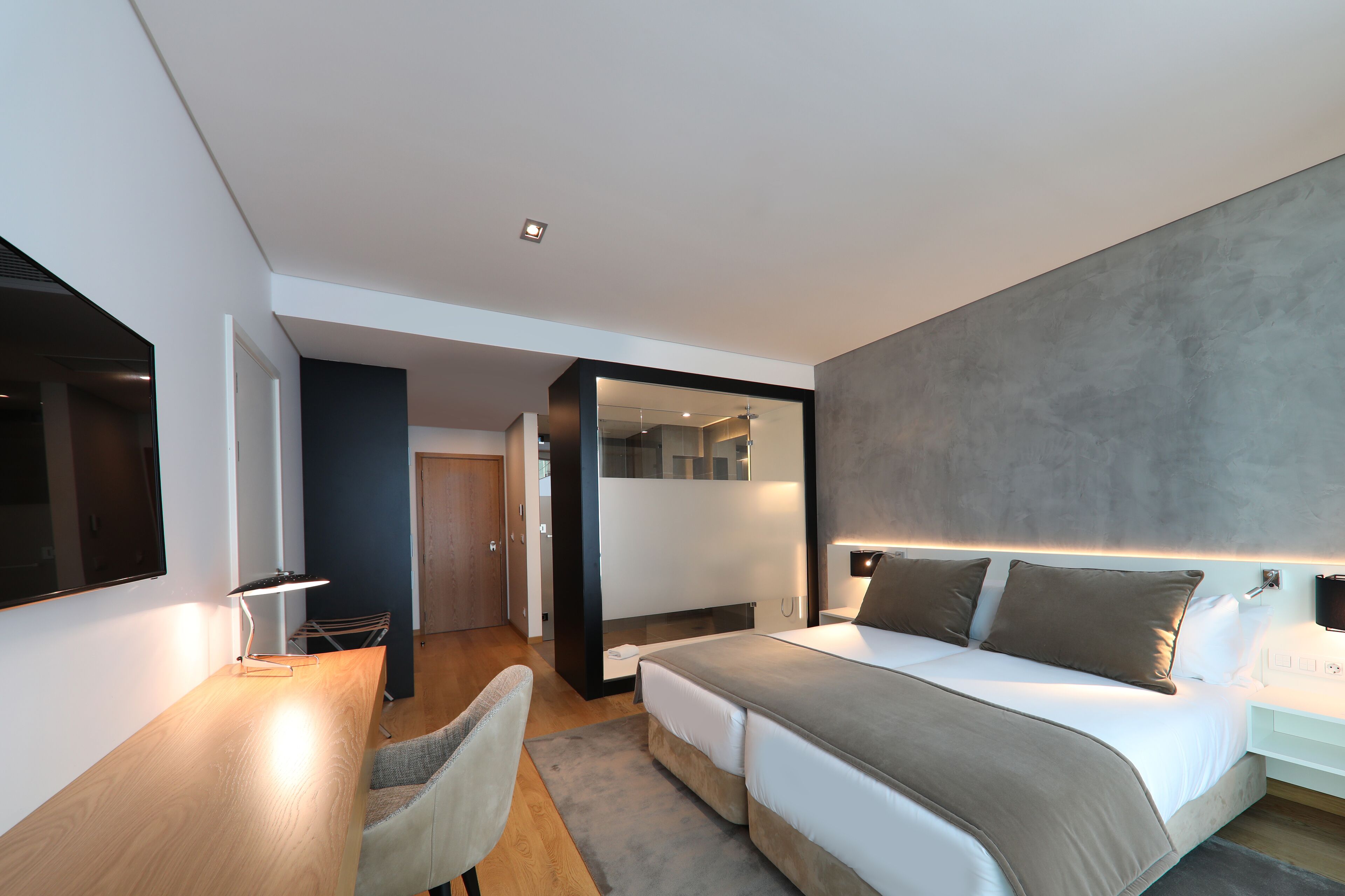 A modern hotel room with a large bed, bedside tables, a desk, and a chair.