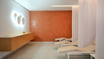 A modern spa room with a reception desk, a wall-mounted light fixture, and several lounge chairs.