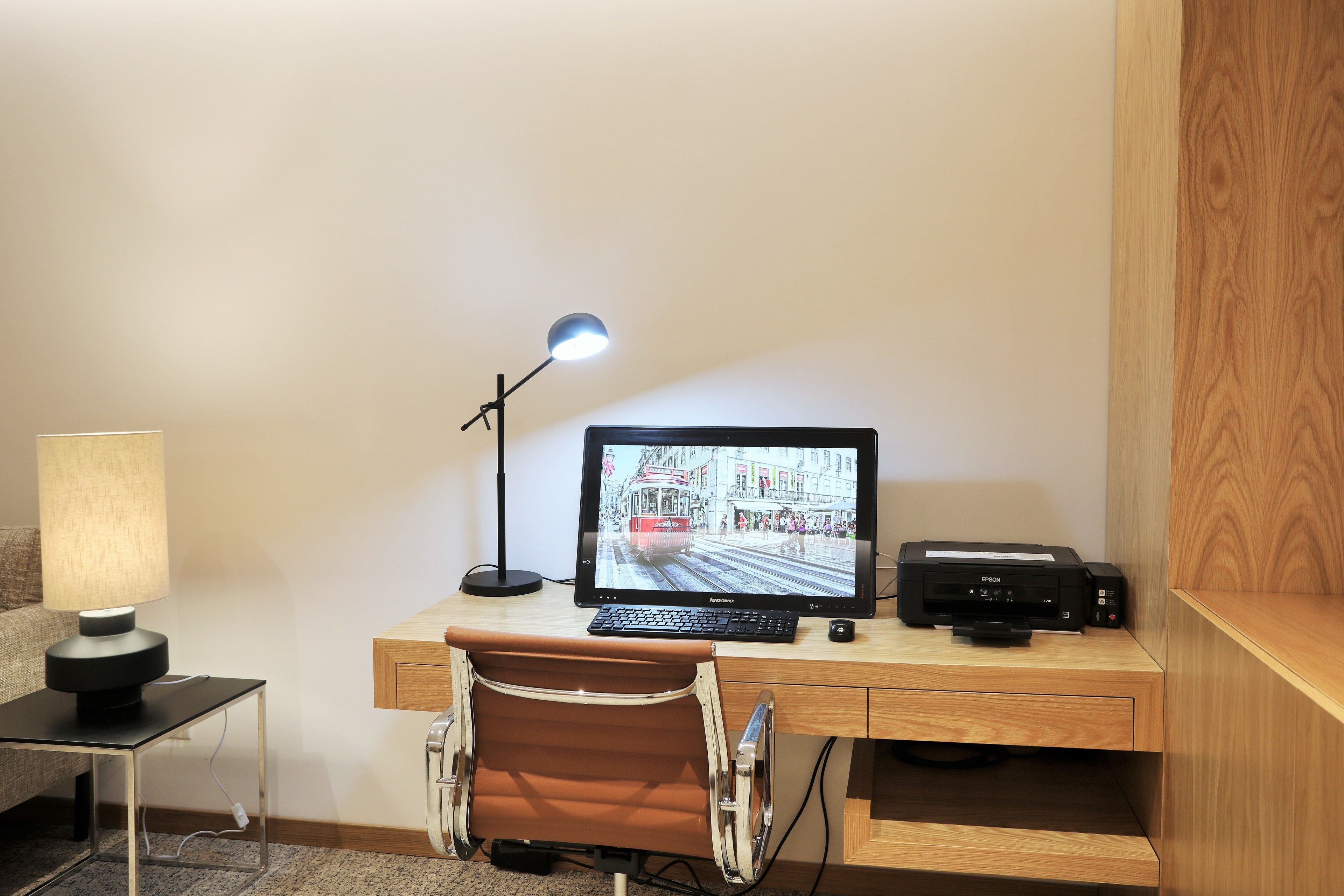 A neatly organized workspace with a desk, chair, lamp, and a computer monitor displaying a cityscape.