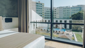 Une chambre d’hôtel moderne dotée d’un grand lit, d’un téléviseur fixé au mur et d’une grande fenêtre donnant sur une piscine et les bâtiments environnants.