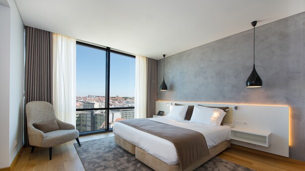 Une chambre d’hôtel moderne, dotée d’un grand lit, d’un fauteuil, d’un bureau et offrant une vue sur la ville.