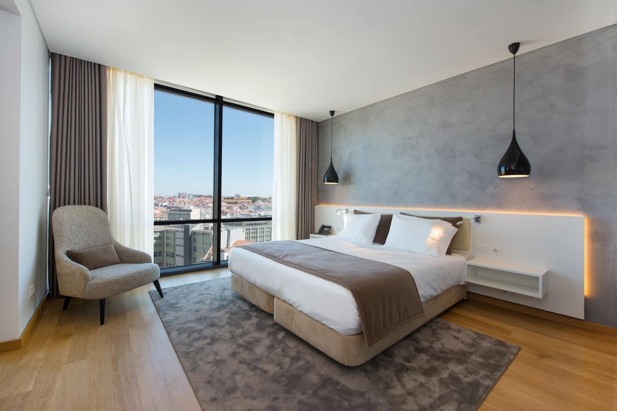 Een moderne hotelkamer met een groot bed, een stoel, een bureau en uitzicht op de stad.