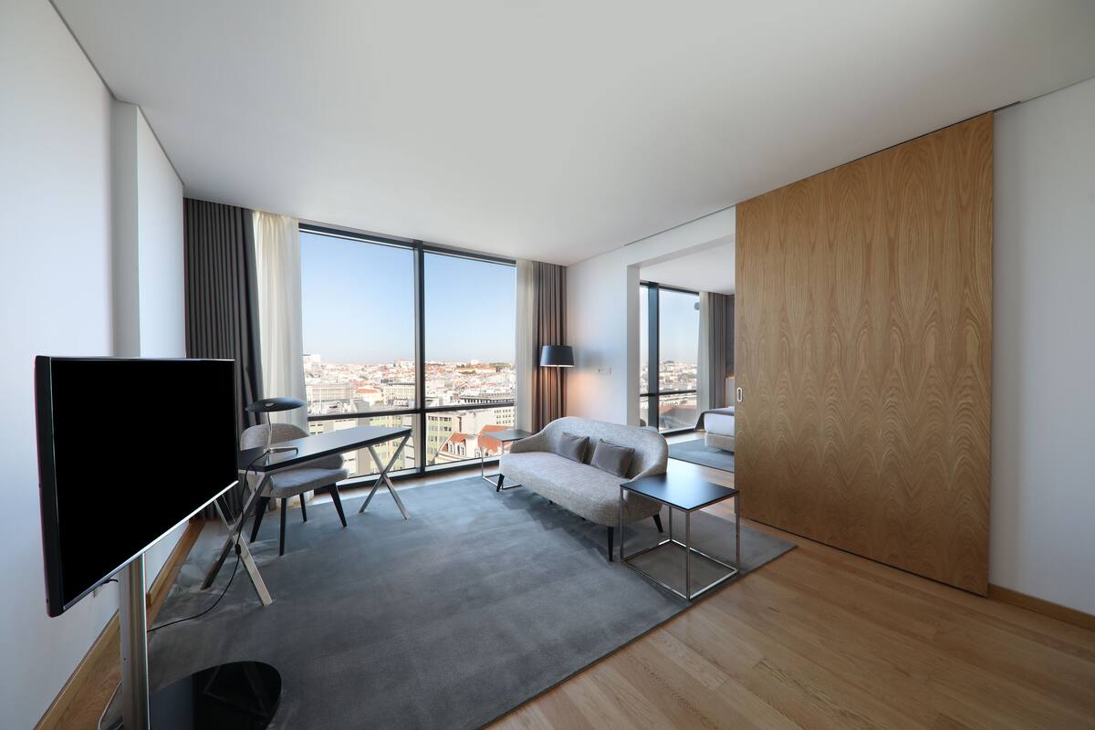 Een moderne hotelkamer met een groot raam, een flatscreen televisie, een bank, een tafeltje en een lamp.
