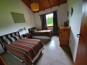 A room with two beds, a wooden cabinet, a desk, and a window with curtains. - Cabañas Normana Inn (El Calafate)