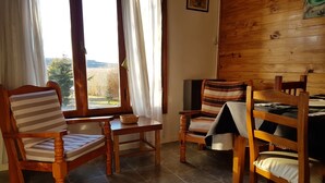 A cozy room with wooden furniture, a window with curtains, and a view of the outdoors. - Cabañas Normana Inn (El Calafate)