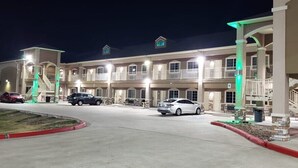Un hotel de varios pisos con un patio central, múltiples balcones y un estacionamiento con varios coches.