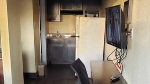 Ett kompakt kök med mörkt trägolv, en matplats med bord och stolar samt en tv som är monterad på väggen.