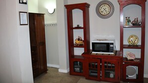 A living room with a wooden cabinet, a microwave, and a clock on the wall. - The Illier's (Westmoorings)
